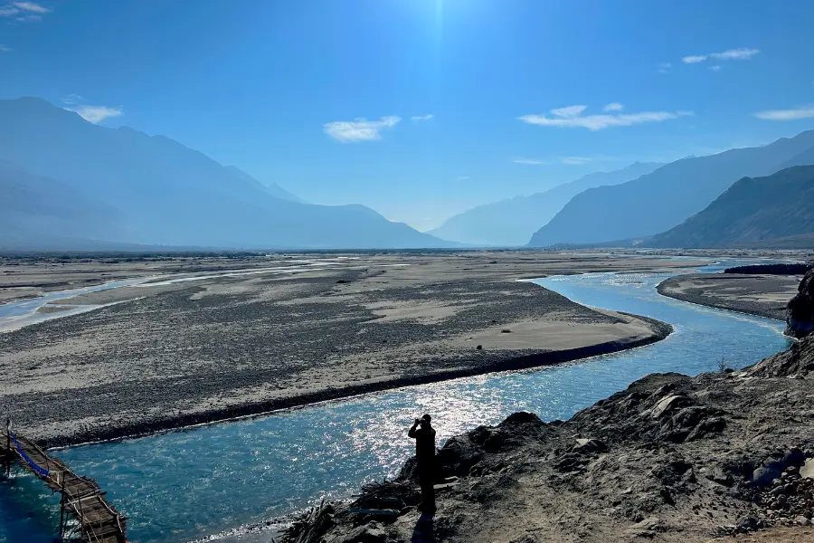 View of river surrounded by mountains under a clear blue sky in the Himalayas.