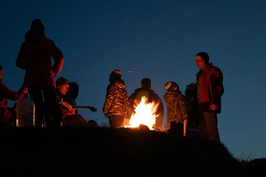 View of trekkers gathered around a campfire at night, enjoying warmth and conversation under the open sky.