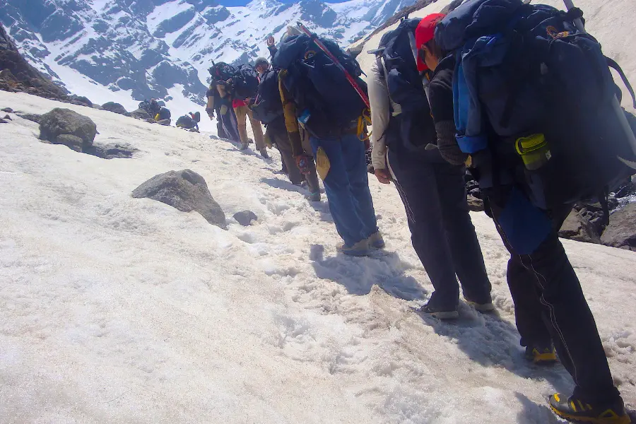 View of group of trekkers ascending a snowy mountain trail with backpacks and gear.