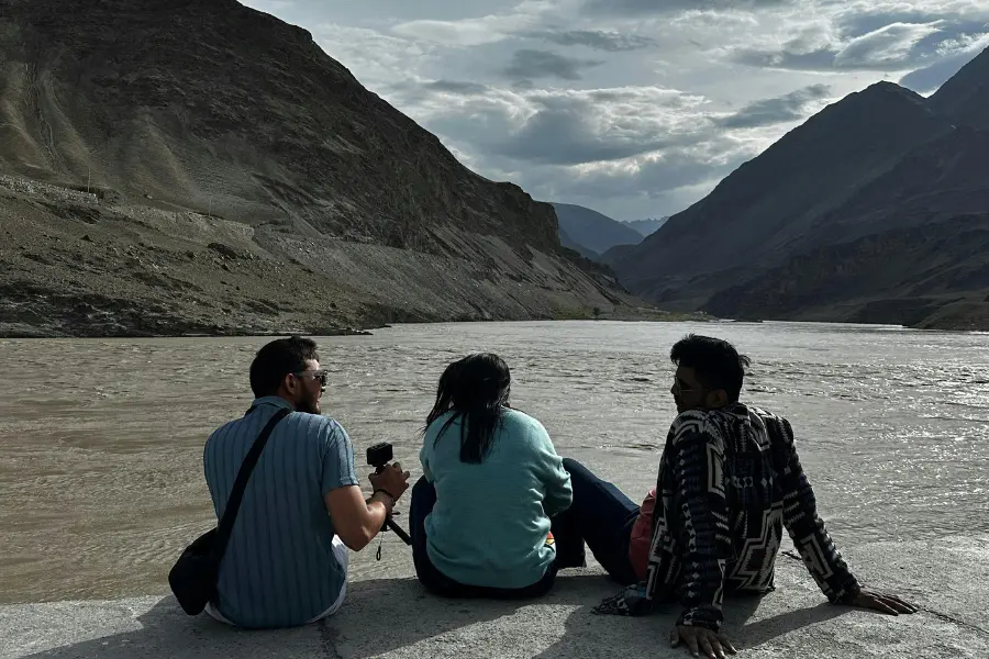 A view of travelers sitting by a river surrounded by rugged mountains.