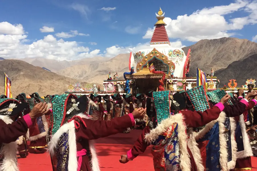View of traditional Ladakhi dancers in vibrant attire performing at a colorful monastery festival surrounded with mountains.