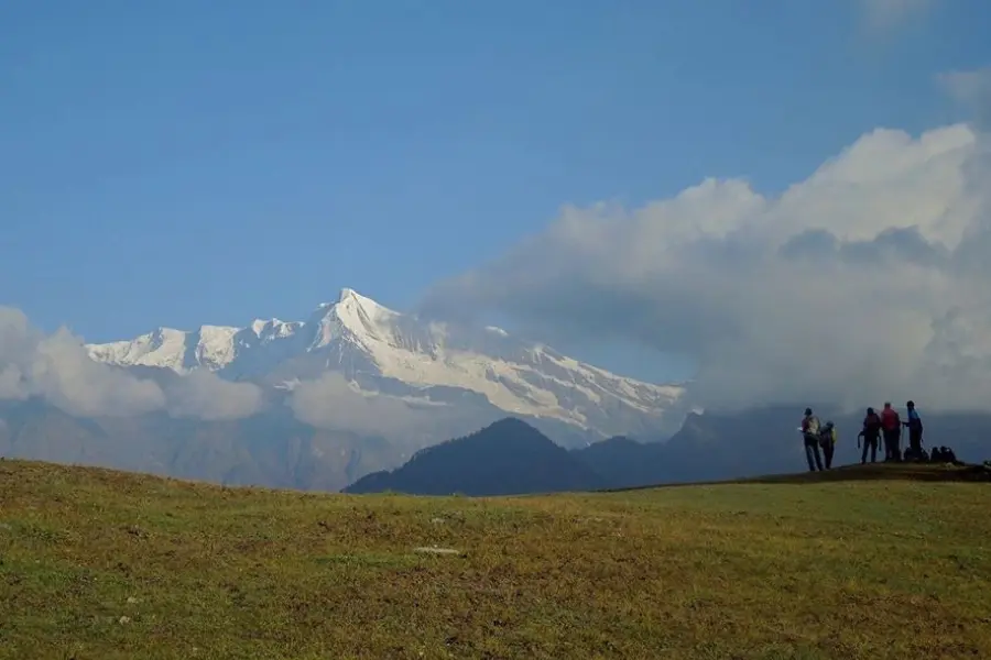 View of trekkers standing on a grassy ridge with Himalayan peaks in the background.